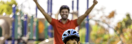 A father cheers on as his son rides a bicycle.