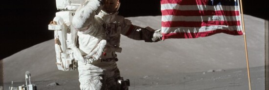 Astronaut Eugene A. Cernan, Apollo 17 commander, is photographed next to the deployed United States flag during lunar surface extravehicular activity (EVA) at the Taurus-Littrow landing site. The highest part of the flag appears to point toward our planet Earth in the distant background. This picture was taken by scientist-astronaut Harrison H. Schmitt, lunar module pilot. While astronauts Cernan and Schmitt descended in the Lunar Module (LM) to explore the moon, astronaut Ronald E. Evans, command module pilot, remained with the Command and Service Modules (CSM) in lunar orbit.