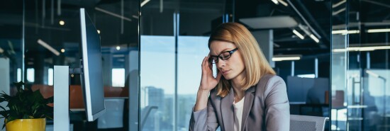Senior business woman has a severe headache while working in a modern office at the computer