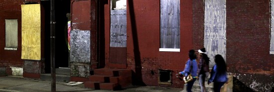 Women walk past blighted row houses in Baltimore.