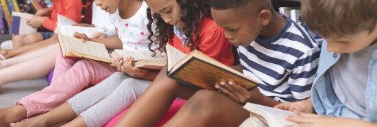 School kids sitting on cushions and studying over books in a library