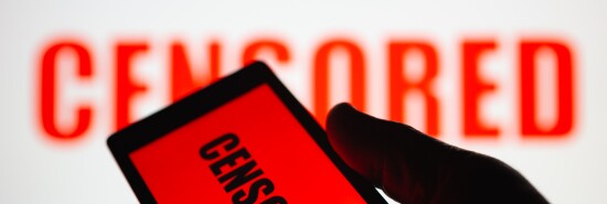 A smartphone in hand displaying the "censored" text. Same text in red blurred on white background. The concept of censorship on popular social networks. Restricted access to internet. Shallow DOF