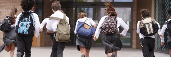 Group Of High School Students Wearing Uniform Running Into School Building At Beginning Of Class