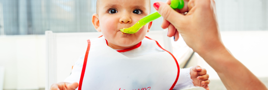 A baby wearing a bib is fed while sitting on a high chair.