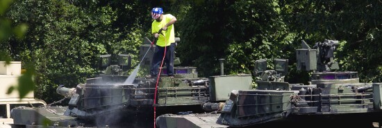 A worker uses pressure washer to clean an Abrams tanks on a flat car in a rail yard in D.C.