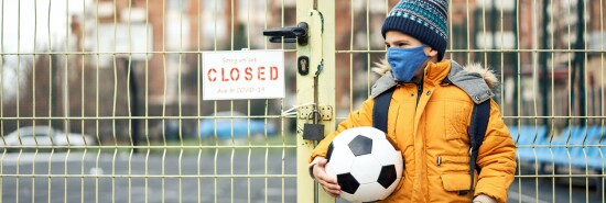 Little boy standing in front of closed playground door with Closed sign