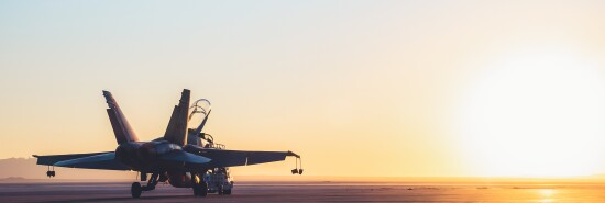 Jet fighter on an aircraft carrier deck against beautiful sunset sky .