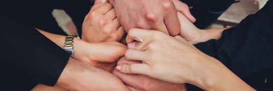 two man and three women holding hands on a table implying a polyamory relationship or love triangle.