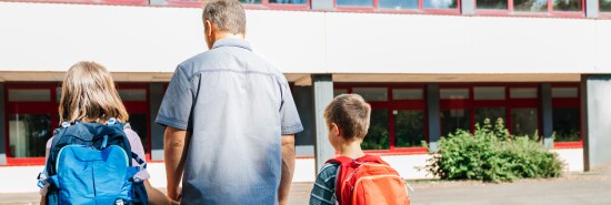 A young father escorts his son and daughter to school. Parental care for children. Back to school. Start of lessons